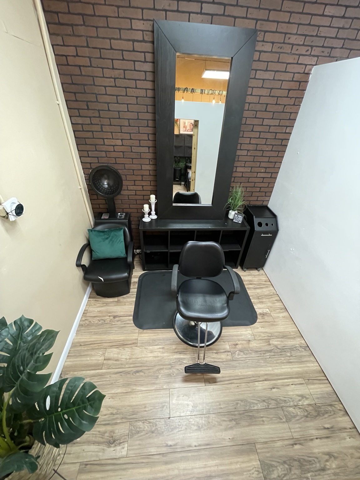 Elevated view of a styling station with a brick accent wall, large mirror, chair, and wood-look floor