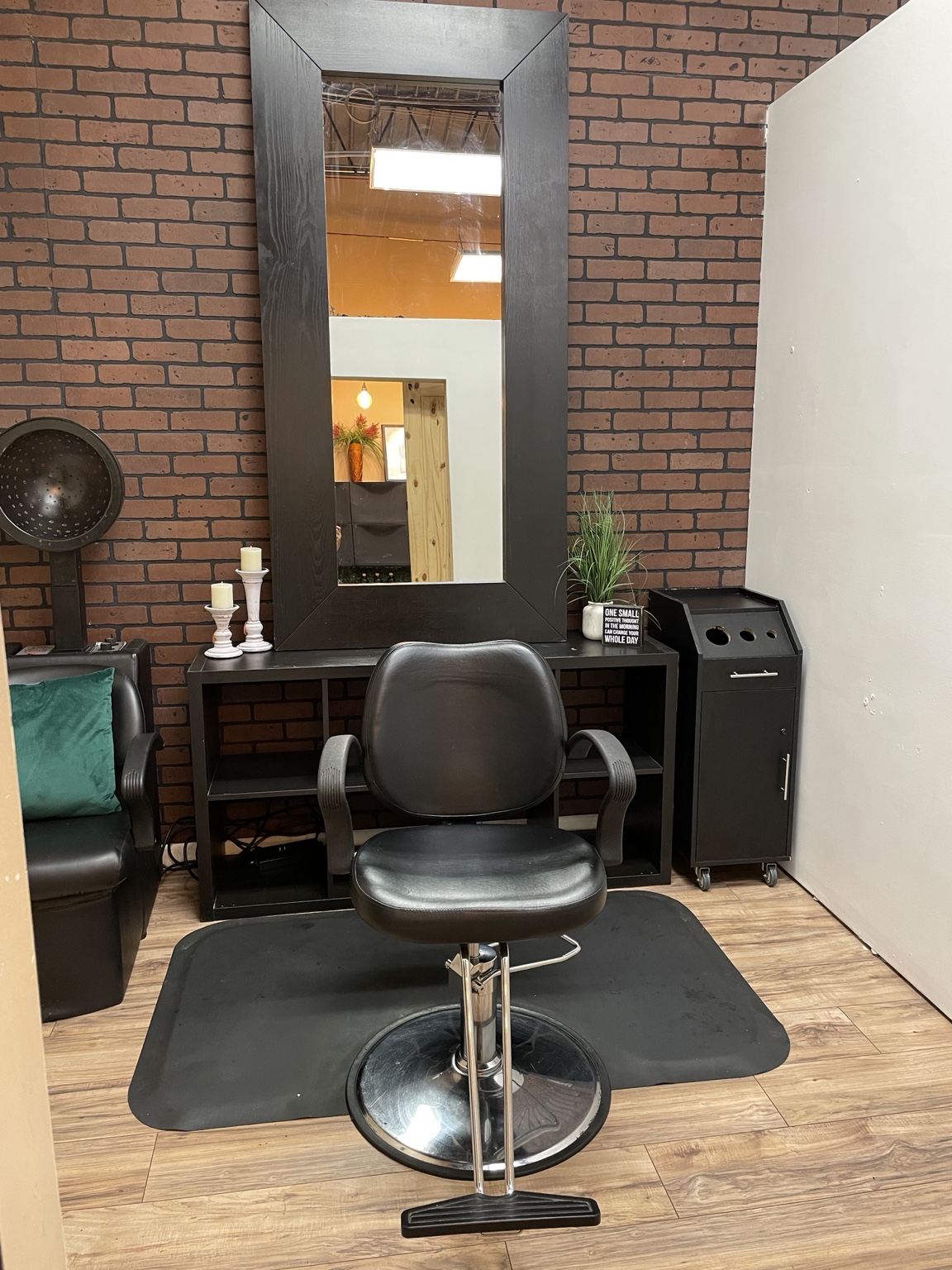Front view of a styling station with a black chair, large mirror, and brick accent wall