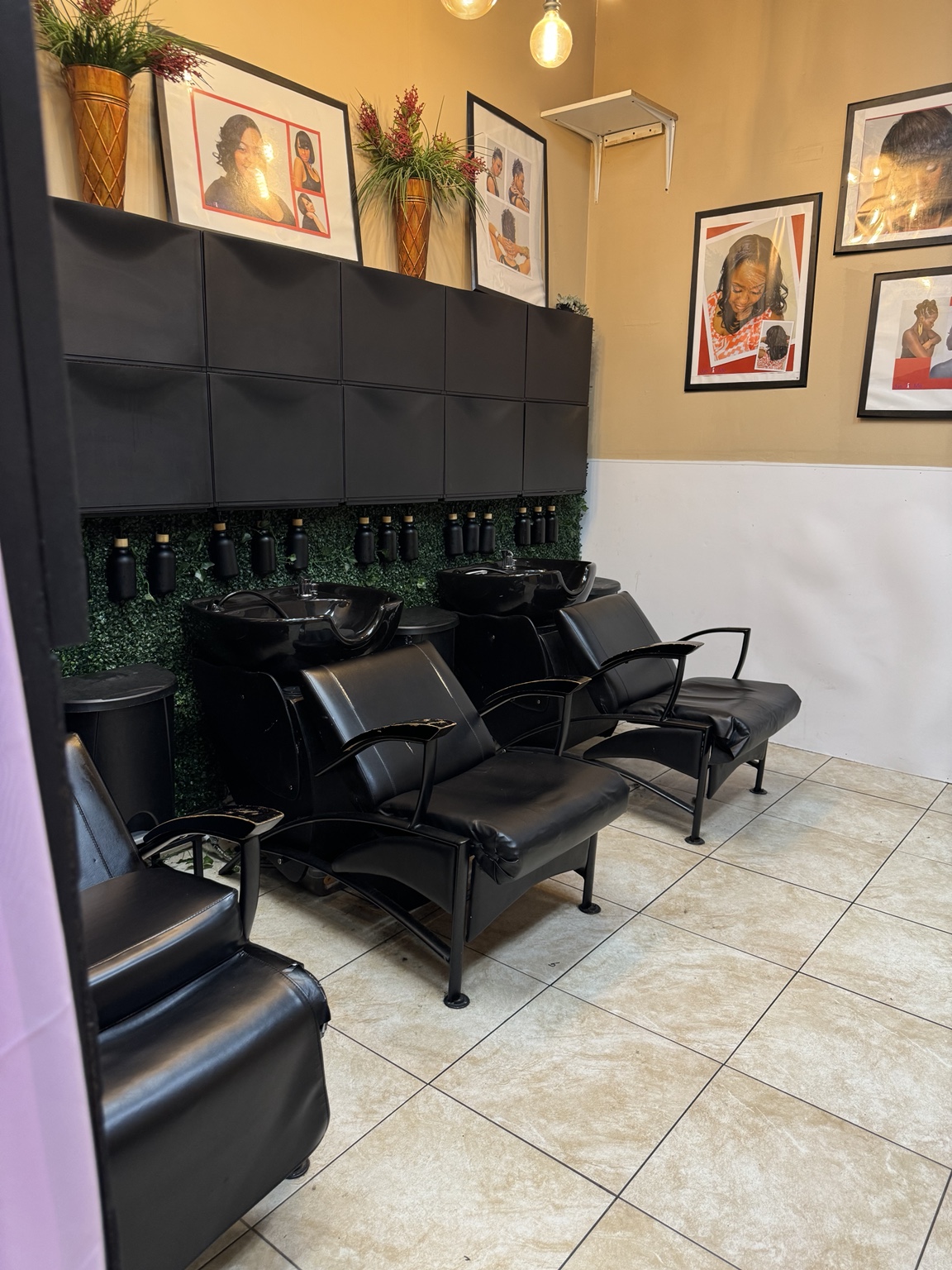 Shared shampoo area with black wash chairs, greenery, cabinets, and framed hairstyle photographs